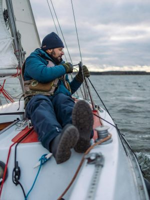 Man sailing a yacht on cold waters with cloudy skies, showcasing adventure.
